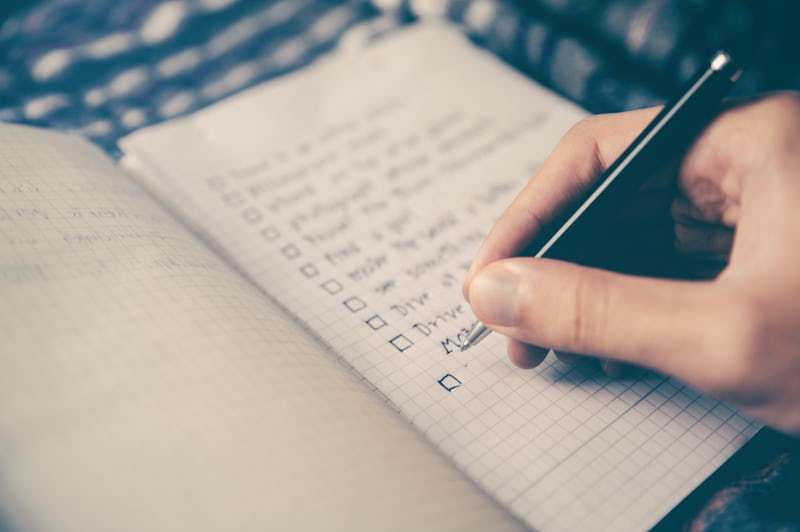 Close-up of a hand holding a pen and checking off items on a to-do list in a notebook.